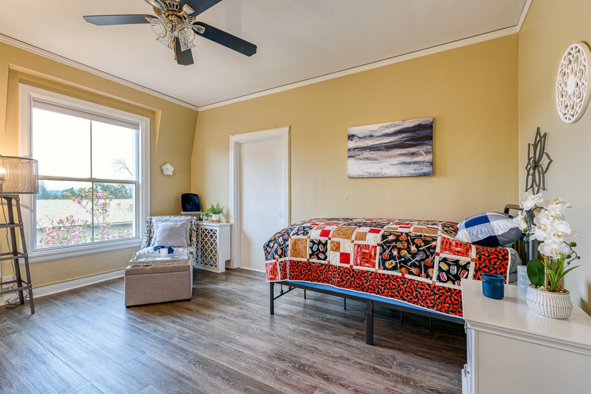 A bright and cozy bedroom featuring a colorful quilt on the bed, modern decor, a large window, and a ceiling fan.