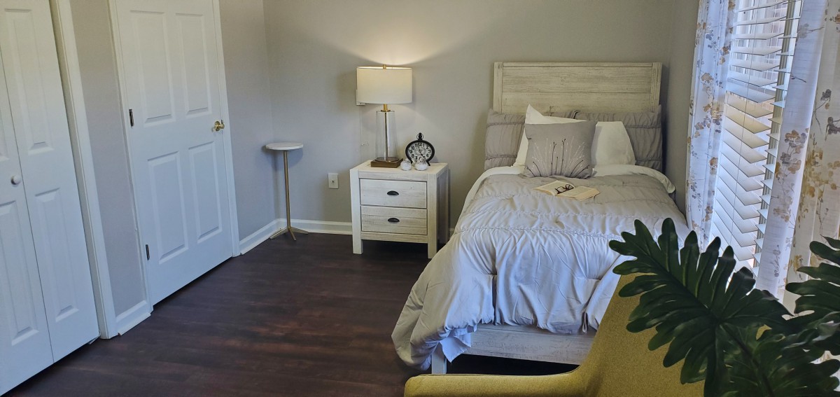 A cozy bedroom with a neatly made bed, nightstand, and soft lighting.