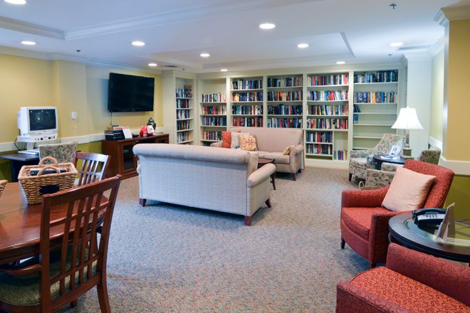 A cozy library space featuring bookshelves, a sofa, chairs, and a television.