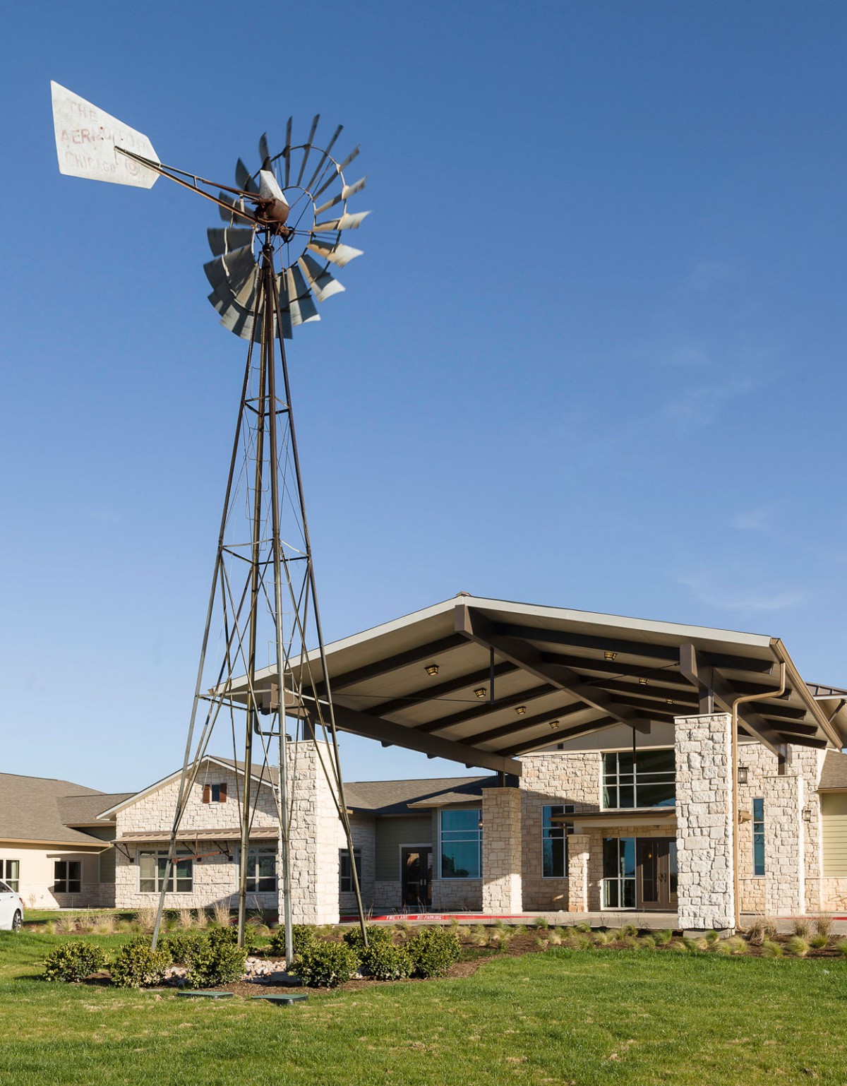 A modern building with a stone facade and an entrance canopy, featuring a windmill against a clear blue sky.