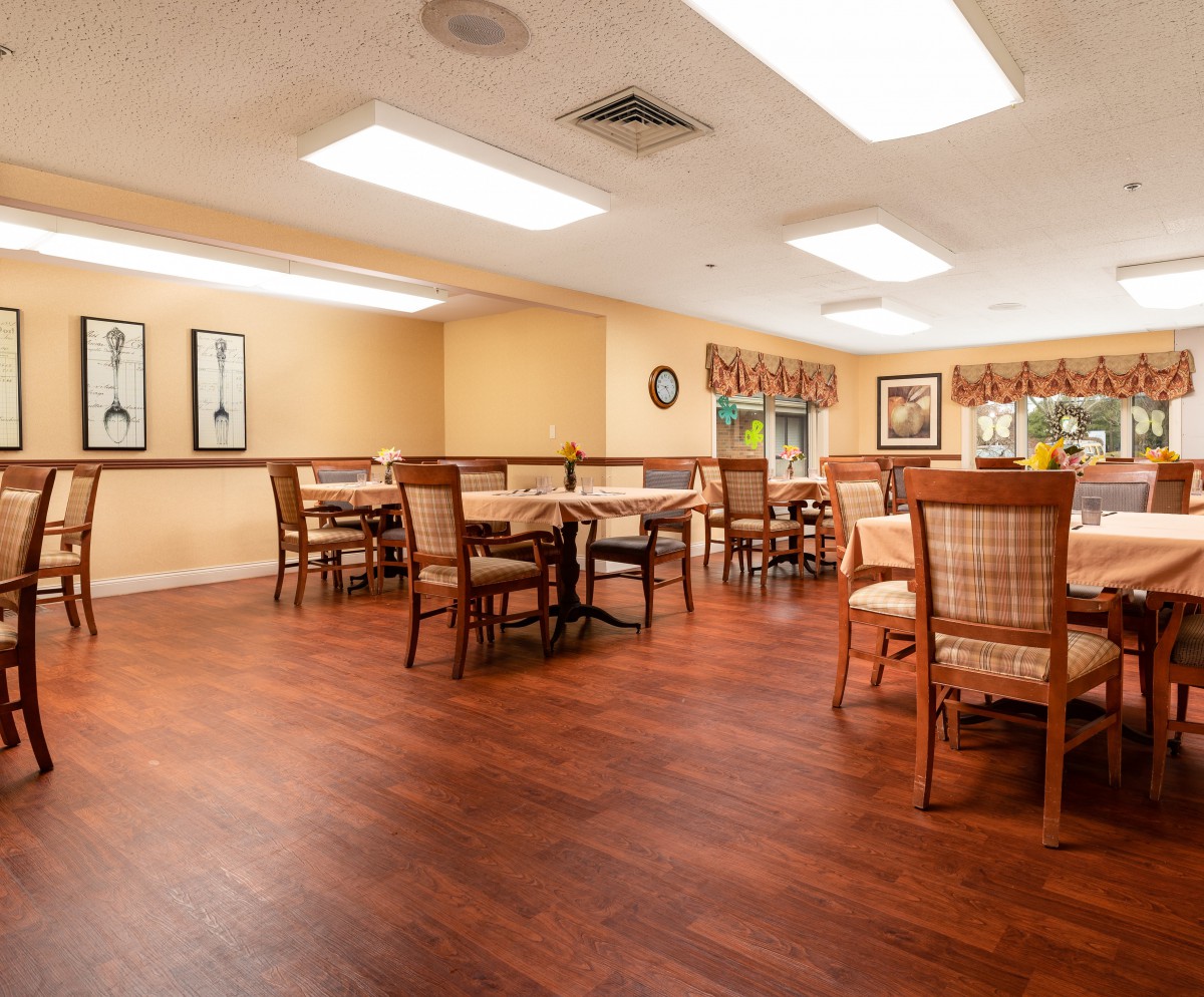 A well-lit dining room with wooden tables and chairs, featuring warm decor and artwork on the walls.