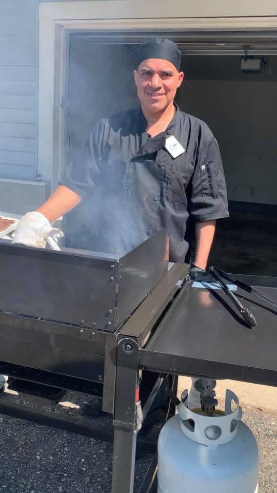 A chef grilling outdoors with smoke rising from the BBQ.
