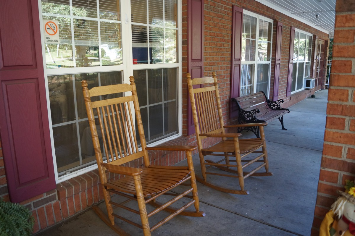 A pair of wooden rocking chairs on a porch with brick walls and large windows.