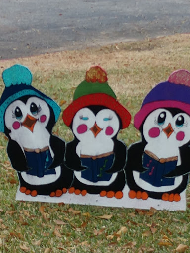 Three adorable penguins wearing colorful hats, enjoying a cozy reading session.