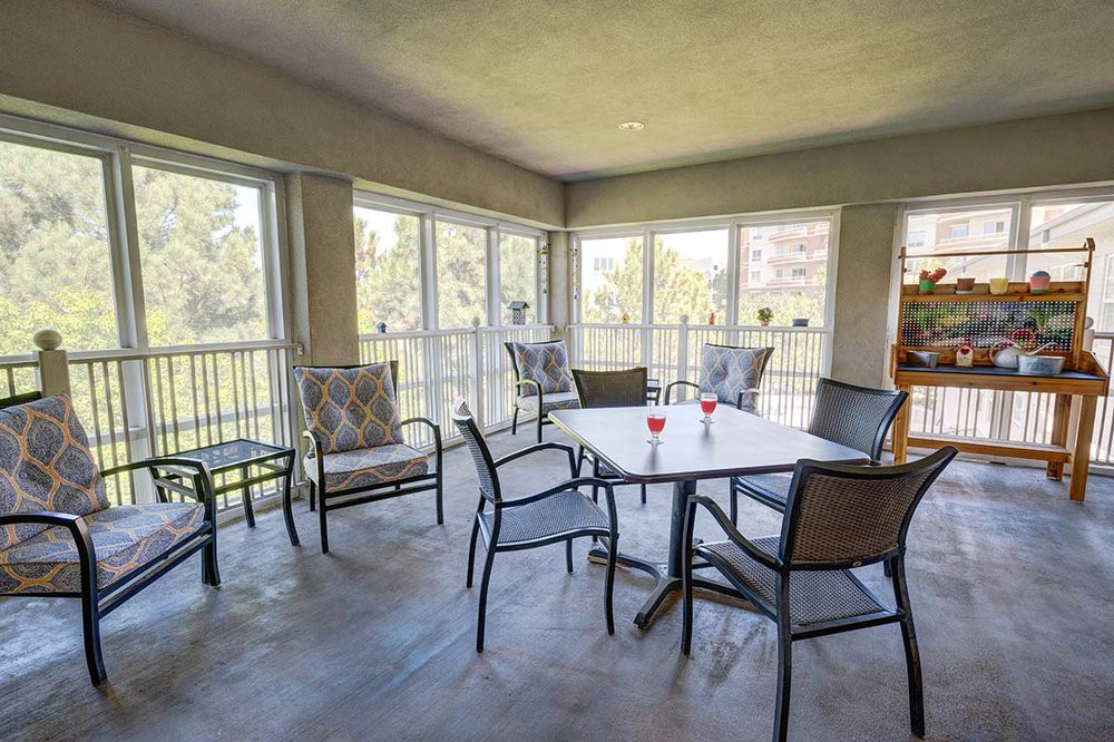 A sunlit dining area with a table and chairs surrounded by large windows.
