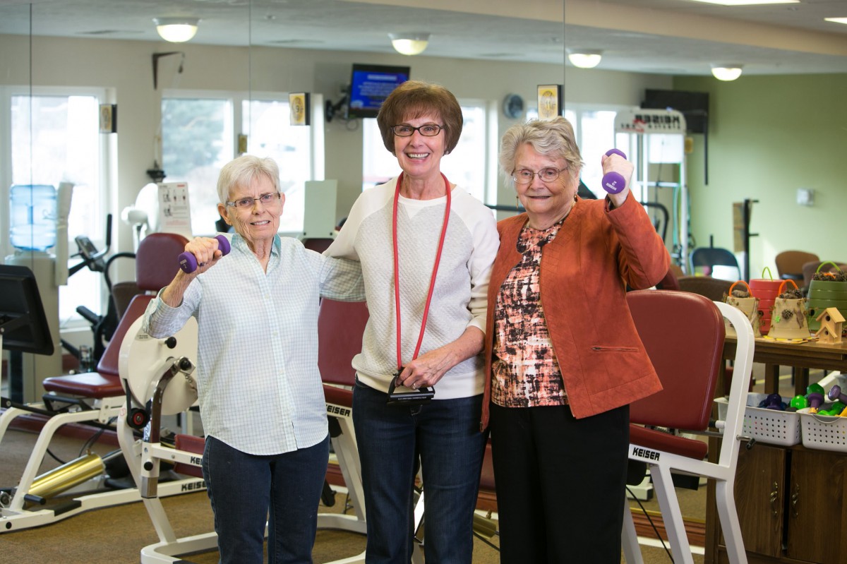 A group of senior women participating in a fitness activity, smiling and holding weights.