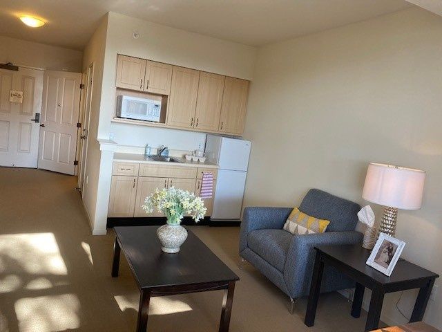 A cozy apartment living room with a kitchenette, featuring a comfortable chair, coffee table, and decorative elements.
