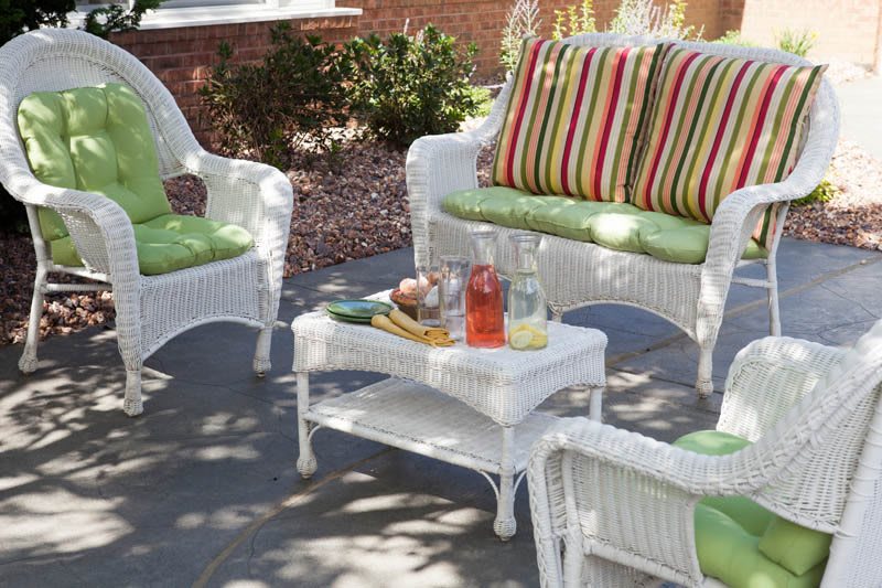A cozy patio setup with white wicker furniture, featuring colorful striped cushions and a small table set for refreshments.