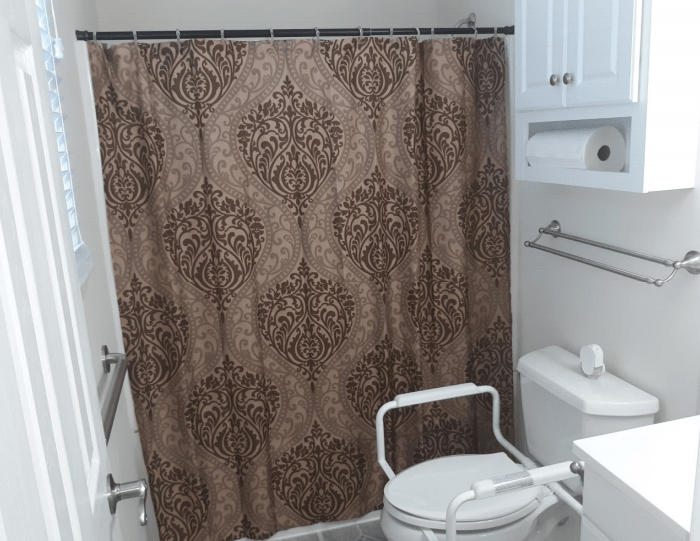 A bathroom with a patterned shower curtain and accessible toilet features.