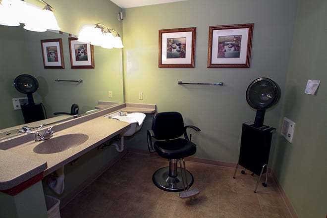 A makeup room with a vanity, chair, and framed artwork on the walls.