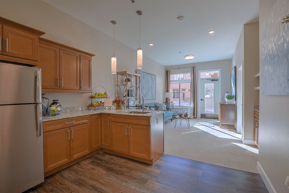 A modern kitchen with wooden cabinets and an open dining area filled with natural light.