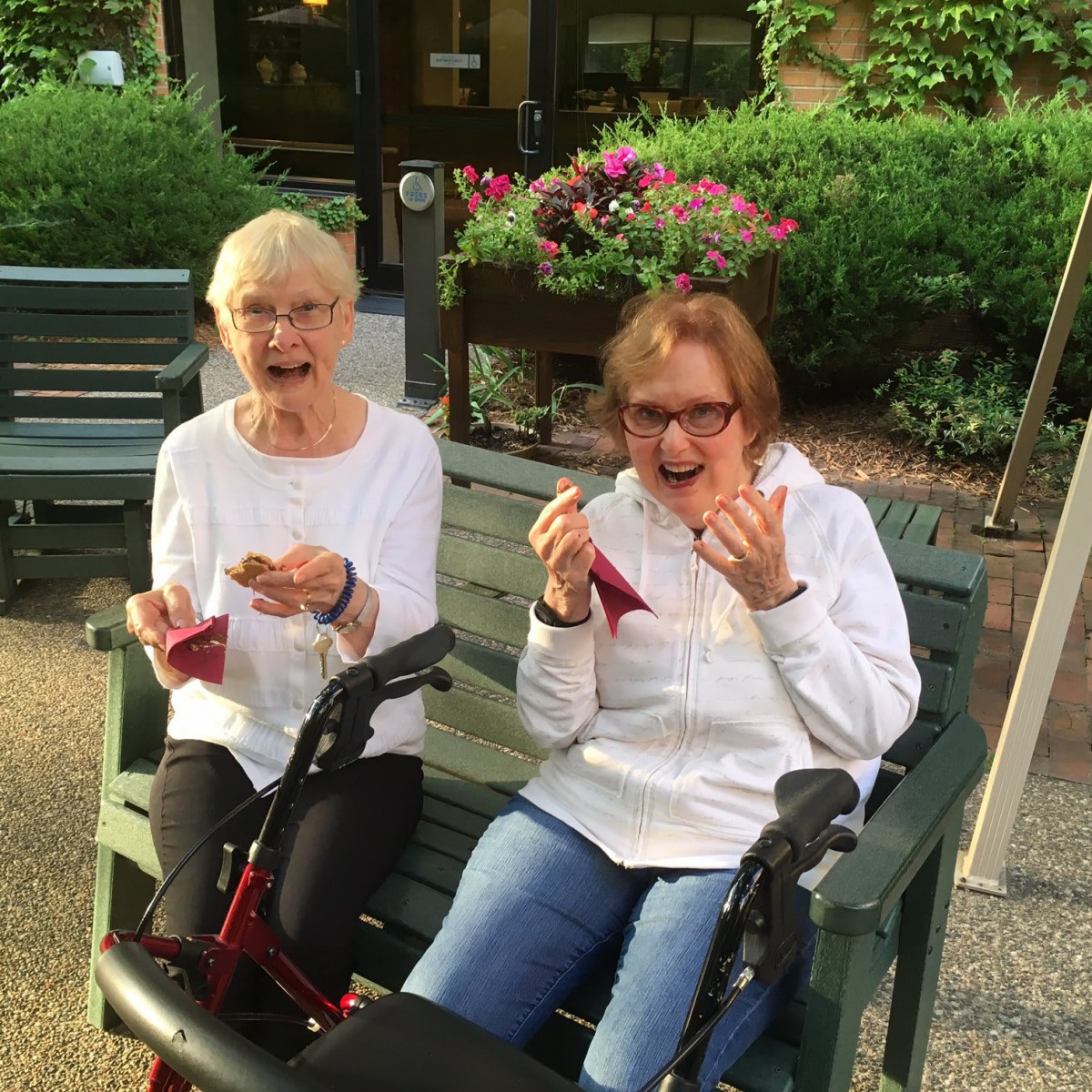 Two elderly women enjoying ice cream on a bench outdoors.