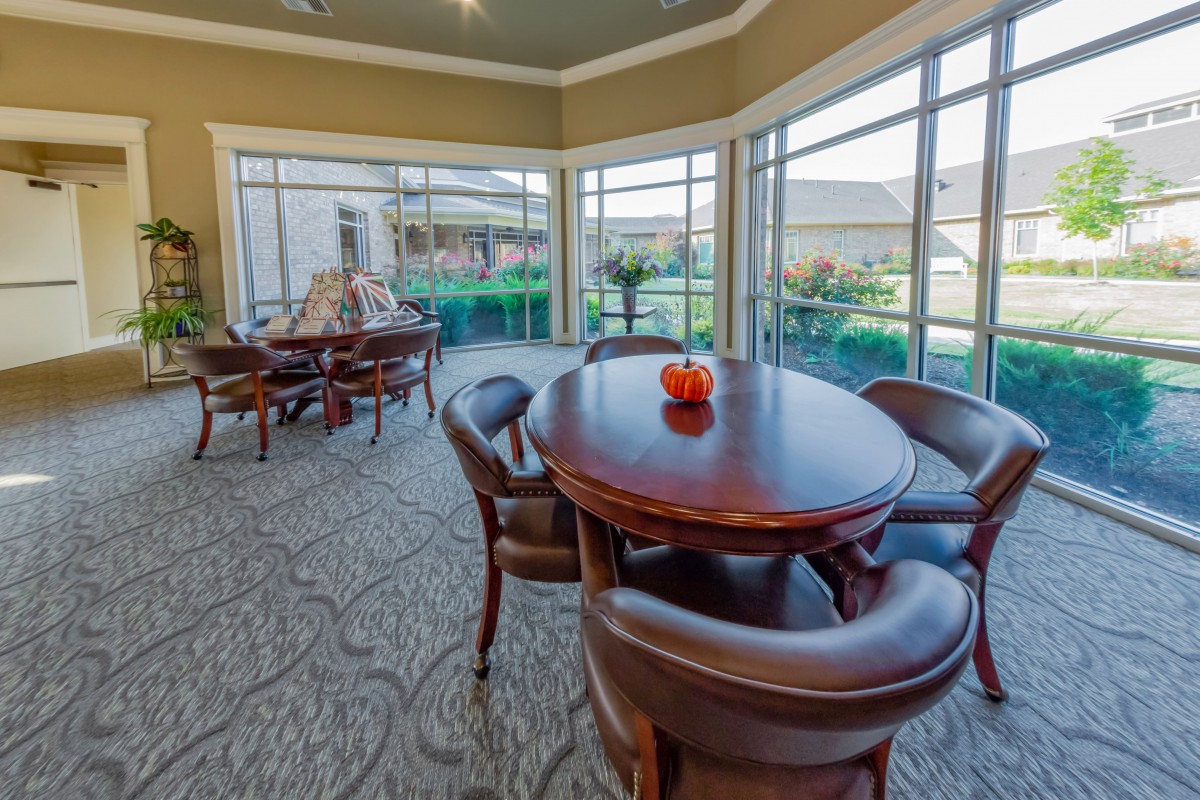 A well-lit dining area with round wooden tables and comfortable chairs, surrounded by large windows offering a view of the outside.
