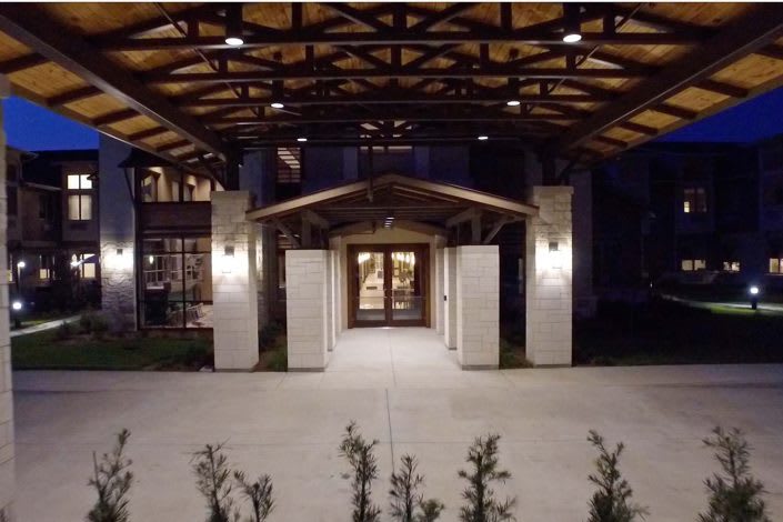A well-lit building entrance at night with a wooden and concrete structure.