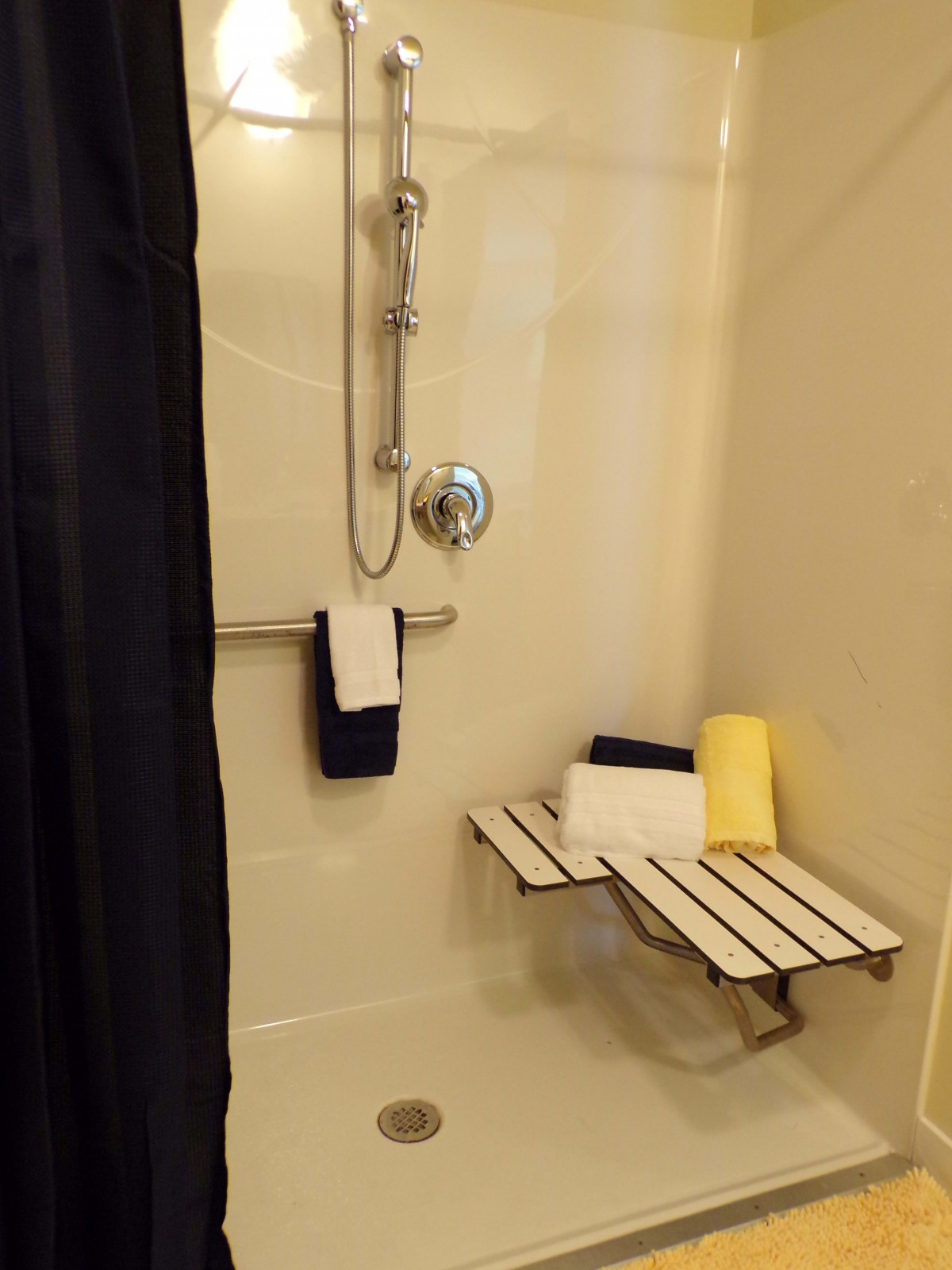 An accessible shower with a wall-mounted bench and towels in a bathroom.