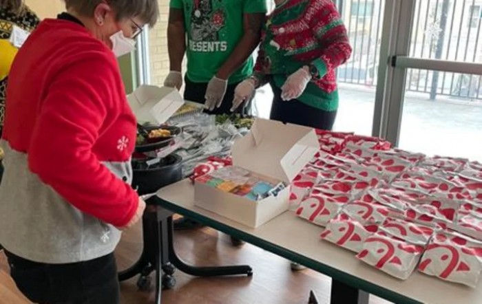 Volunteers wearing festive clothing decorate holiday cookies indoors.