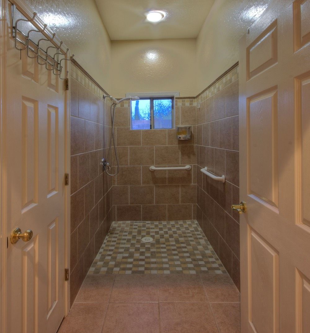 A well-lit bathroom featuring tiled walls and floor with multiple doors leading into the shower area.