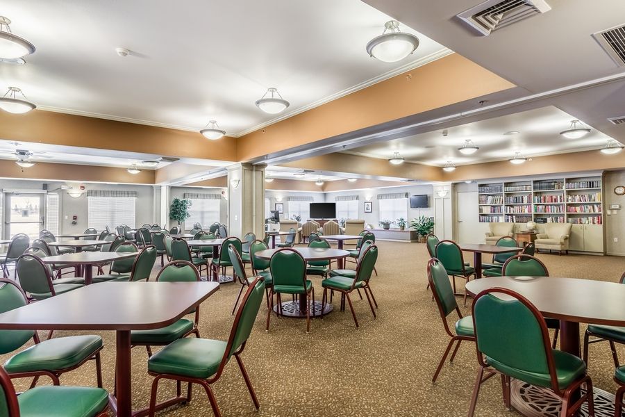 A spacious dining area with multiple tables and chairs, featuring bright lighting and a carpeted floor.