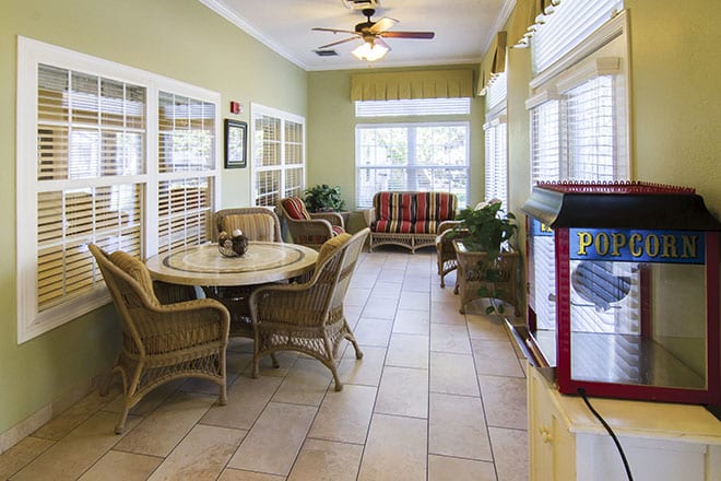A bright sunroom with wicker furniture, large windows, and a popcorn machine.