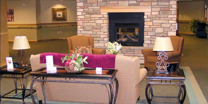 A cozy living room interior featuring a fireplace, comfortable sofas, chairs, and floral decorations.