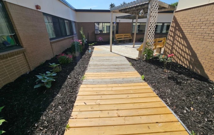 A wooden walkway leading through a garden with a pergola and outdoor seating.