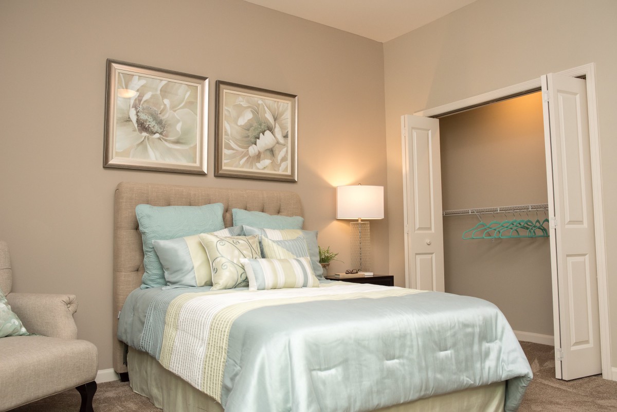 A cozy bedroom featuring a neatly made bed with multiple pillows and soft linens, complemented by wall artwork and a warm lamp.