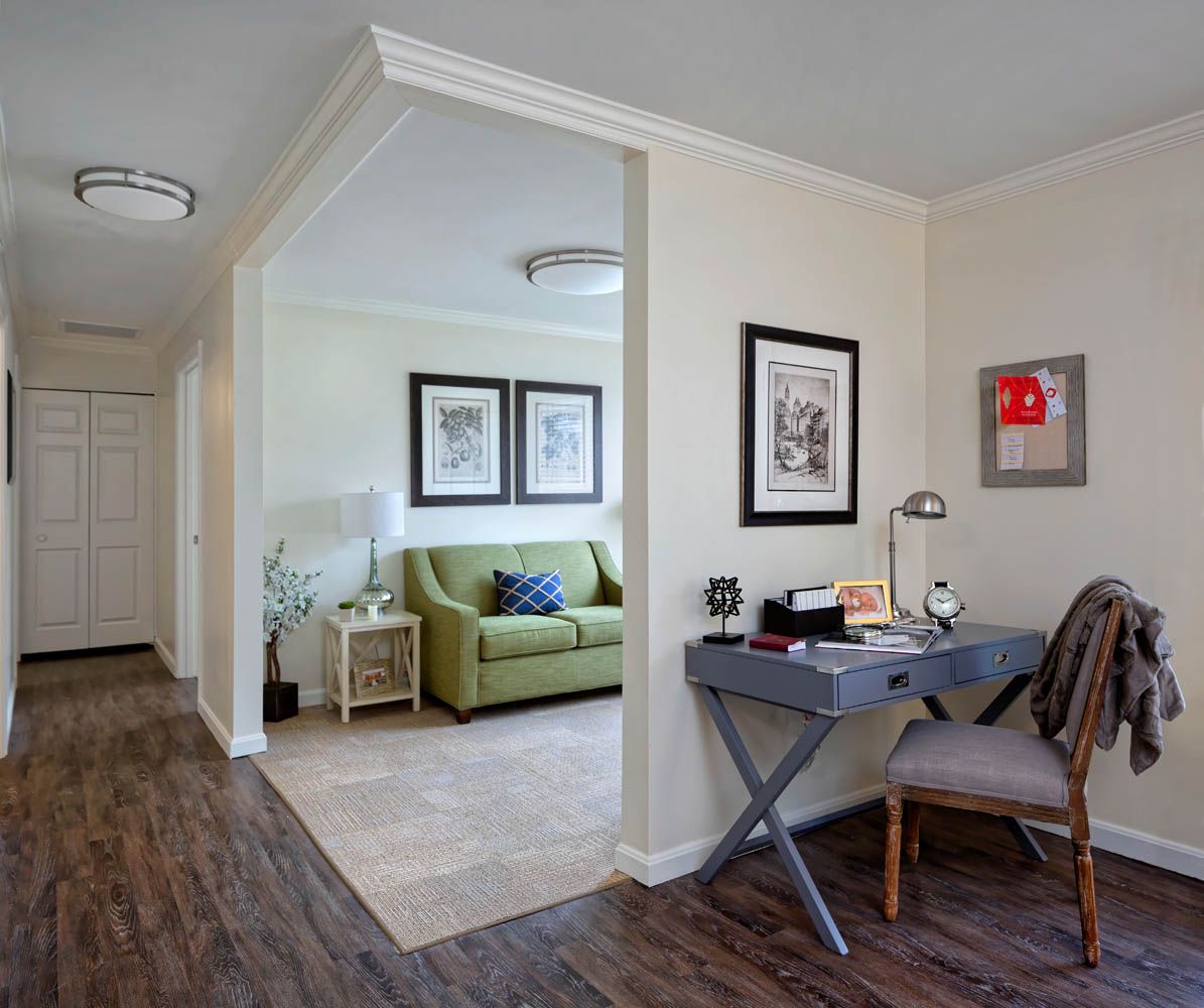 A cozy living space with a green sofa, desk area, and artwork on the walls.