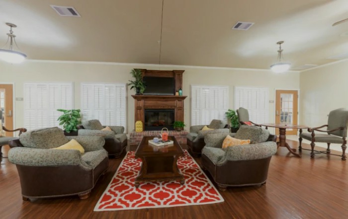 A cozy living room with multiple sofas, a coffee table, and a fireplace, accented by a vibrant red patterned carpet and green plants.