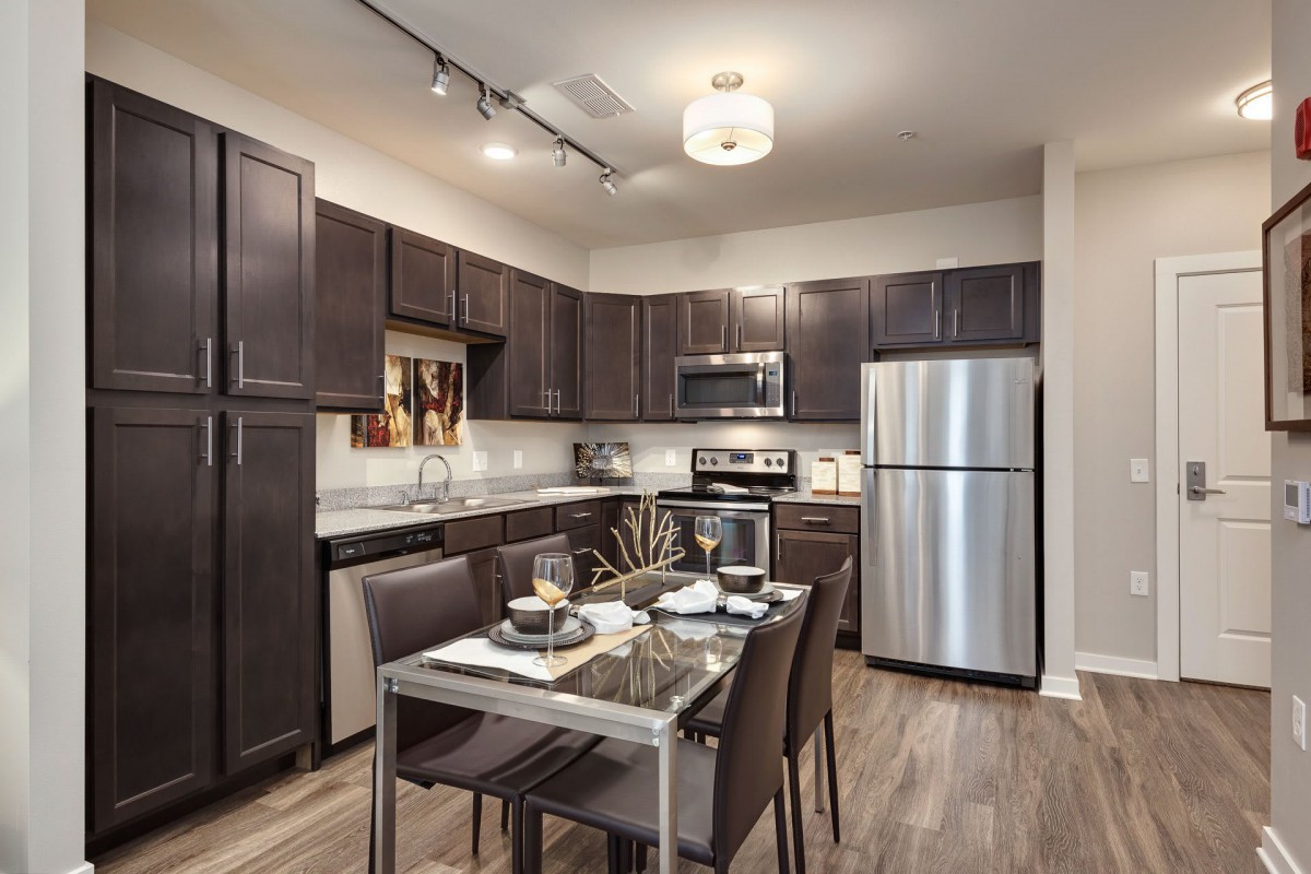 A modern kitchen with dark wood cabinets, stainless steel appliances, and a dining table set for a meal.