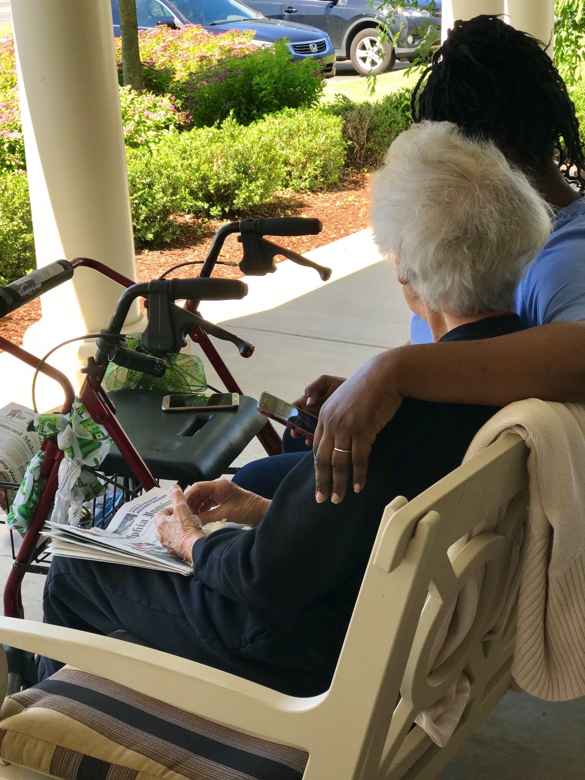 An elderly person sits on a bench outdoors with a caregiver by their side, showing companionship and support.