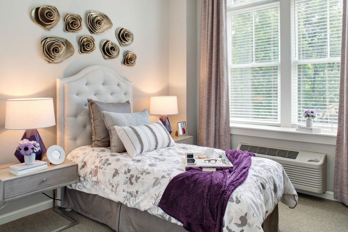 A cozy bedroom with decorative pillows and wall art, illuminated by natural light.