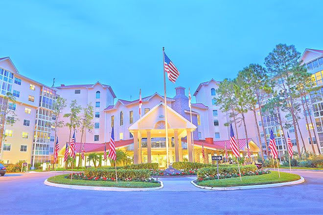 A brightly lit hotel entrance with multiple flags and surrounding trees.