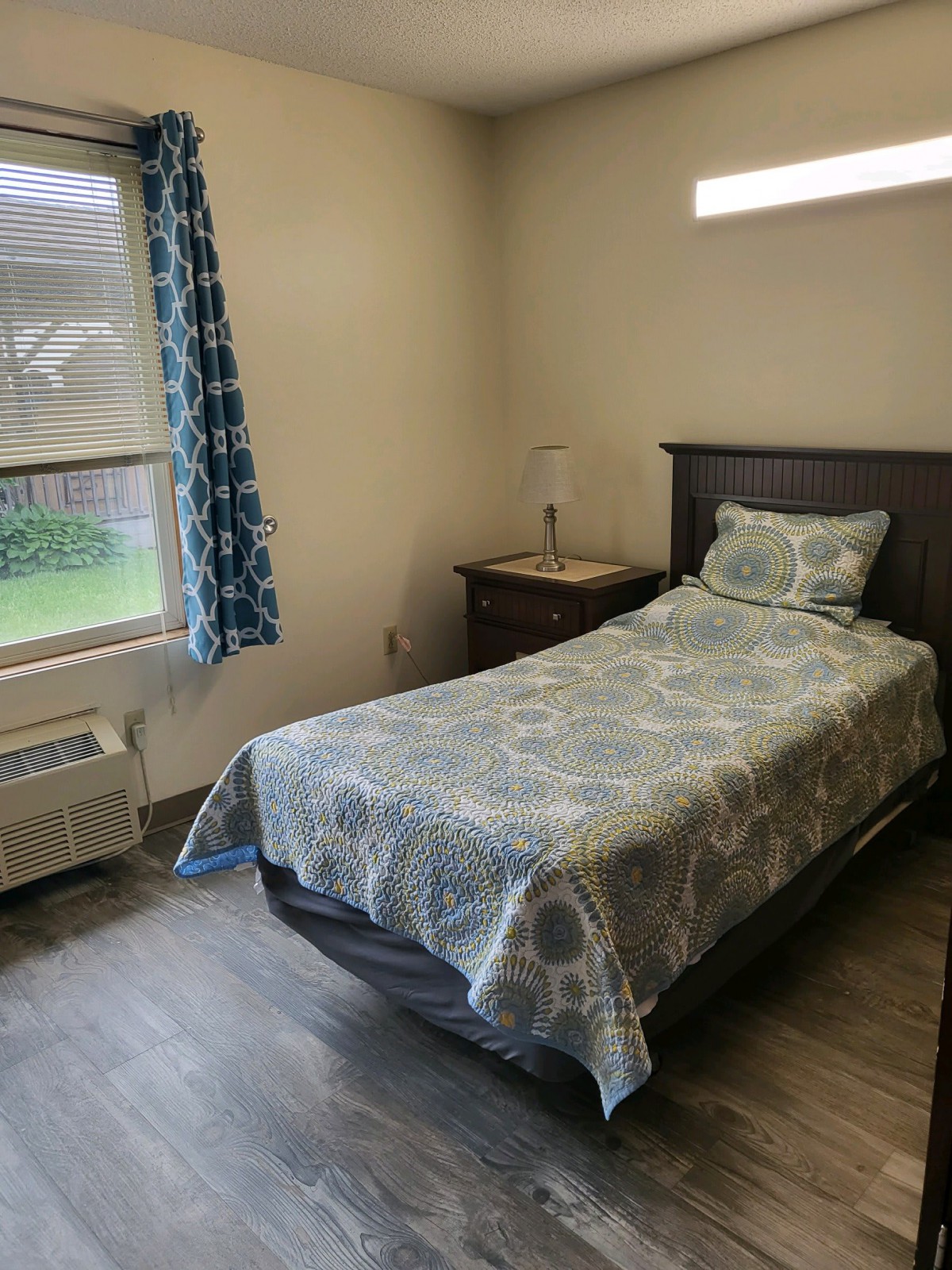 A neatly arranged bedroom with a single bed, nightstand, and window with curtains.