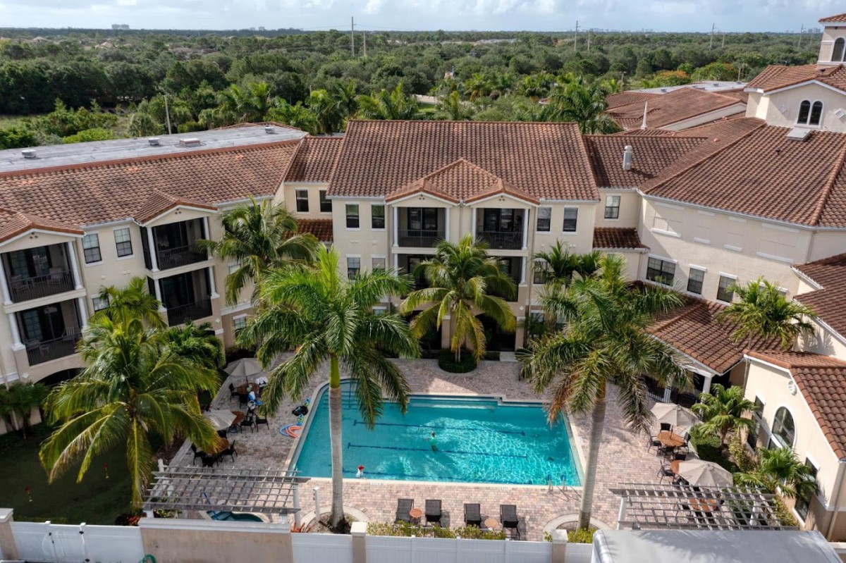 Aerial view of a residential complex with a central swimming pool surrounded by palm trees and lush greenery.
