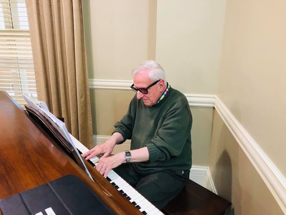 An elderly person playing the piano indoors.