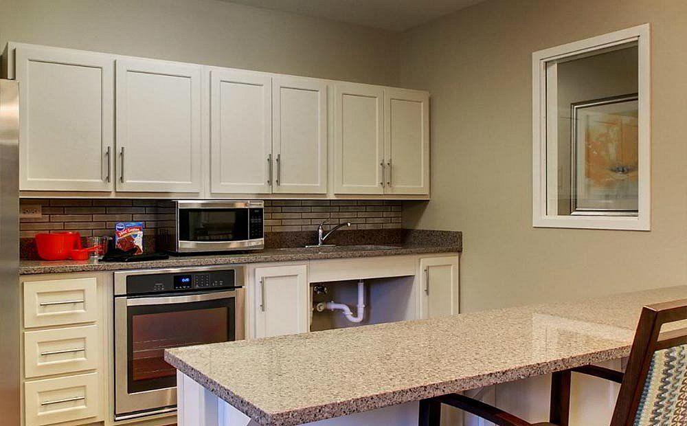 A modern kitchen with white cabinets, a granite countertop island, and built-in appliances.