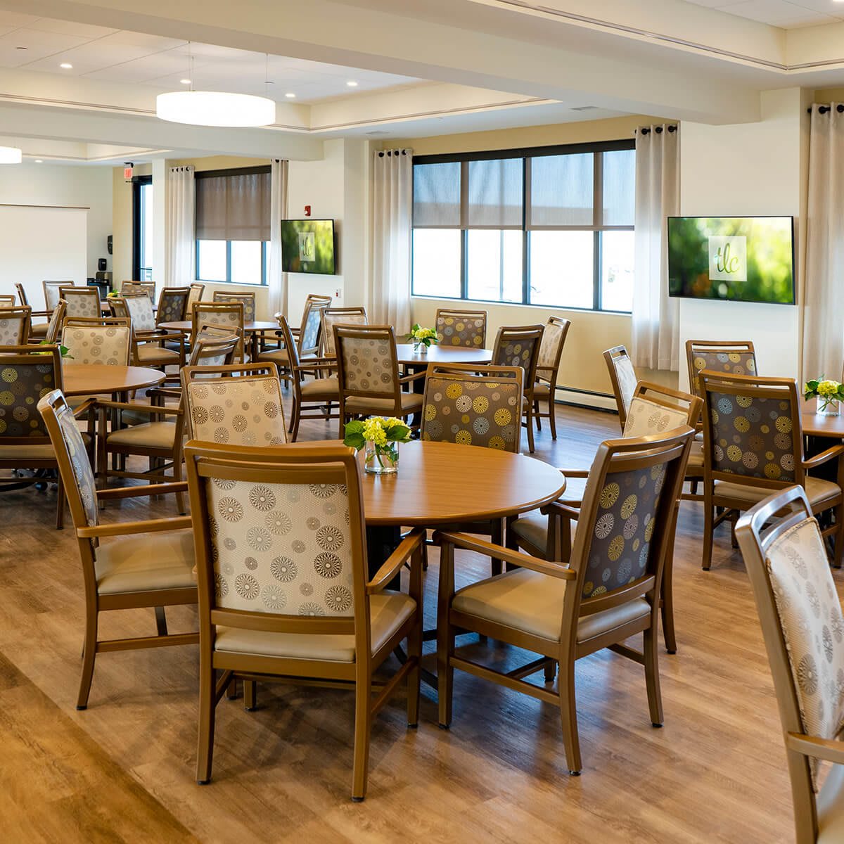 A modern dining area with neatly arranged tables and chairs, featuring large windows for natural light.