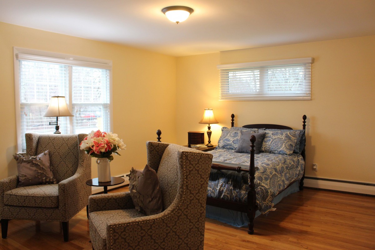 A cozy bedroom with a bed, two chairs, and a flower vase.