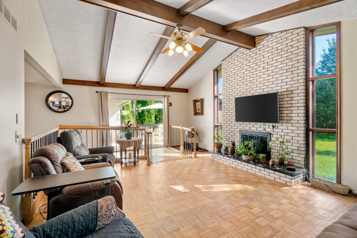 Spacious living room with a vaulted ceiling, exposed beams, and a brick fireplace.