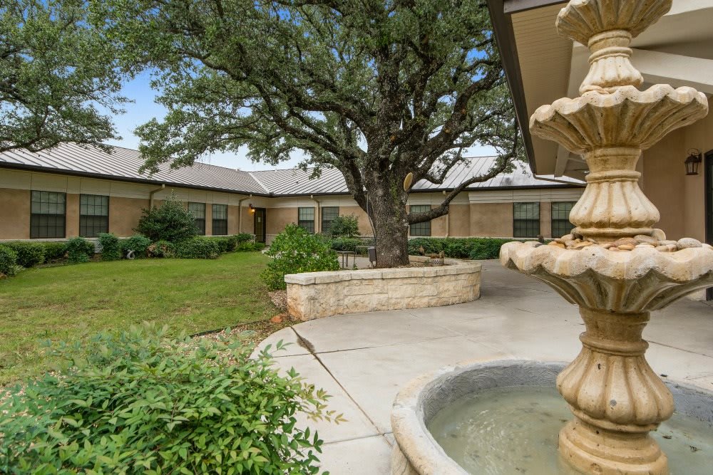 A serene courtyard with a central fountain, surrounded by greenery and buildings.