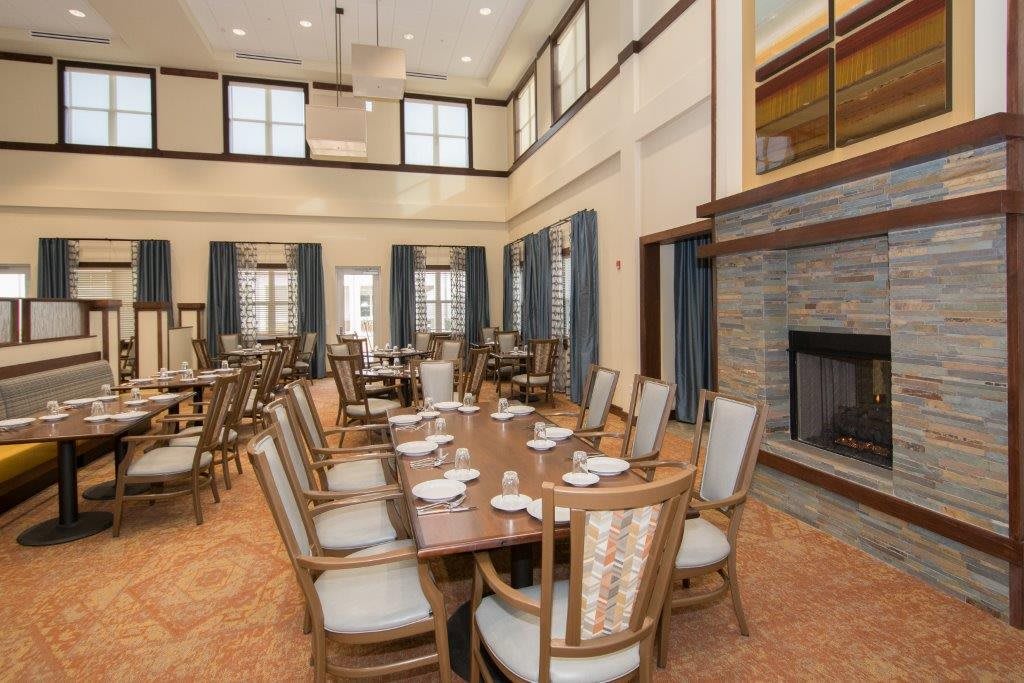 A spacious dining room with multiple tables and chairs, featuring a fireplace and large windows.