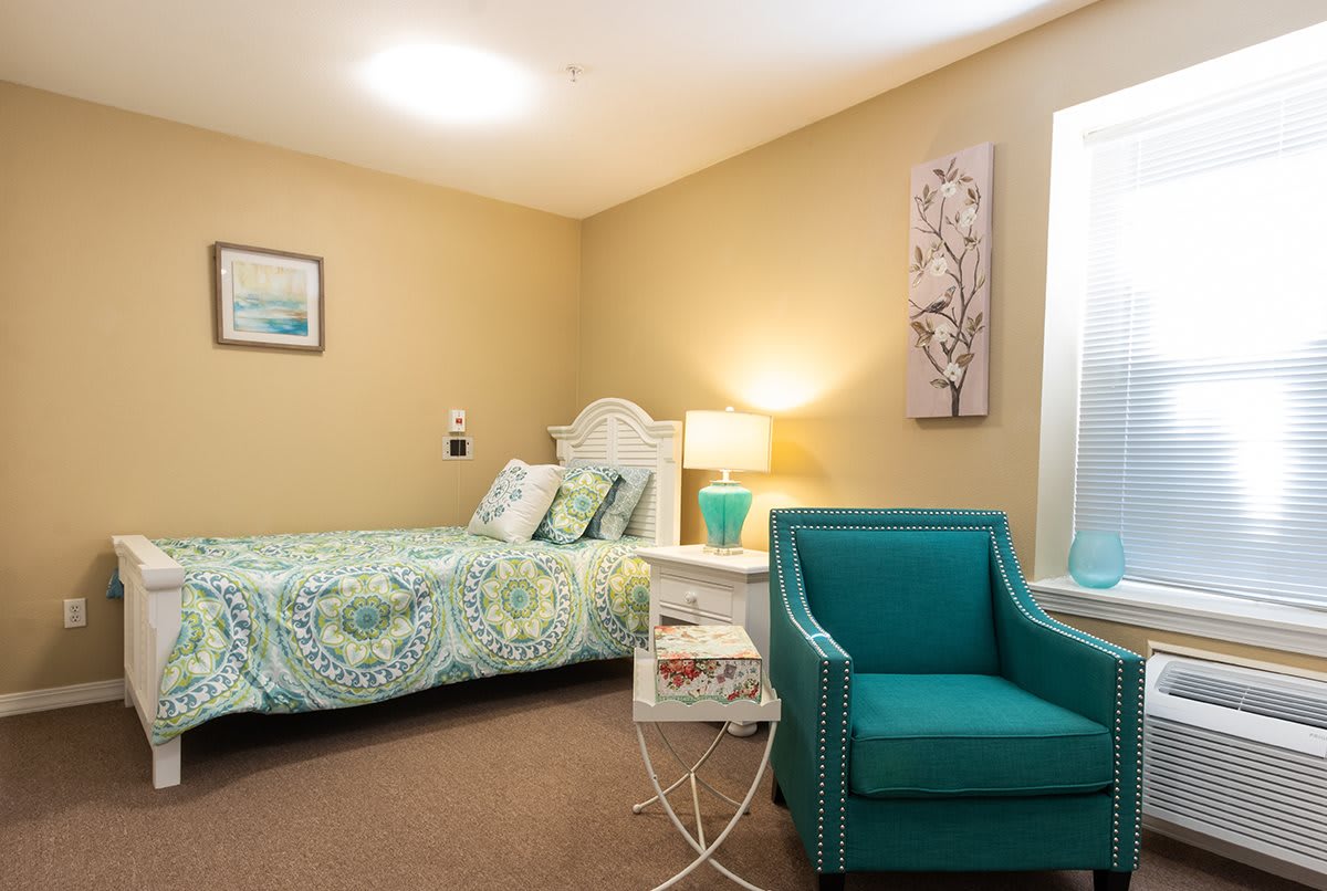 A cozy bedroom with a bed, teal chair, and soft lighting.