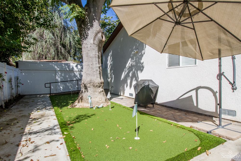 A backyard featuring a putting green with an umbrella and a tree nearby.
