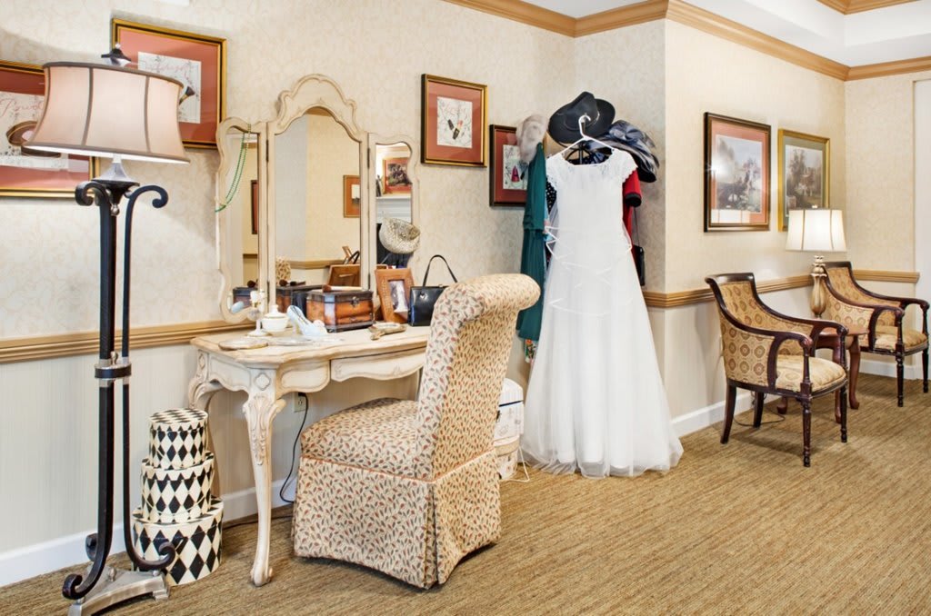 A cozy dressing room featuring a wedding dress on display beside an elegant vanity and chair.