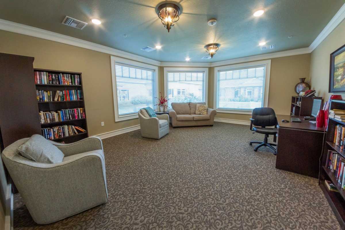 A cozy living room with sofas, armchairs, a bookshelf, and large windows.