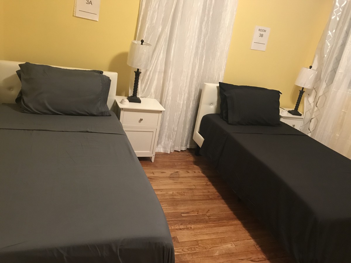A cozy bedroom with twin beds, each accompanied by a nightstand and lamp, set against soft yellow walls.