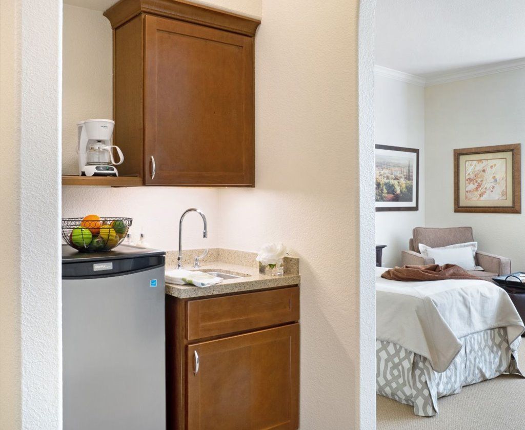 A cozy kitchenette with wooden cabinets and a mini refrigerator, adjacent to a bedroom.