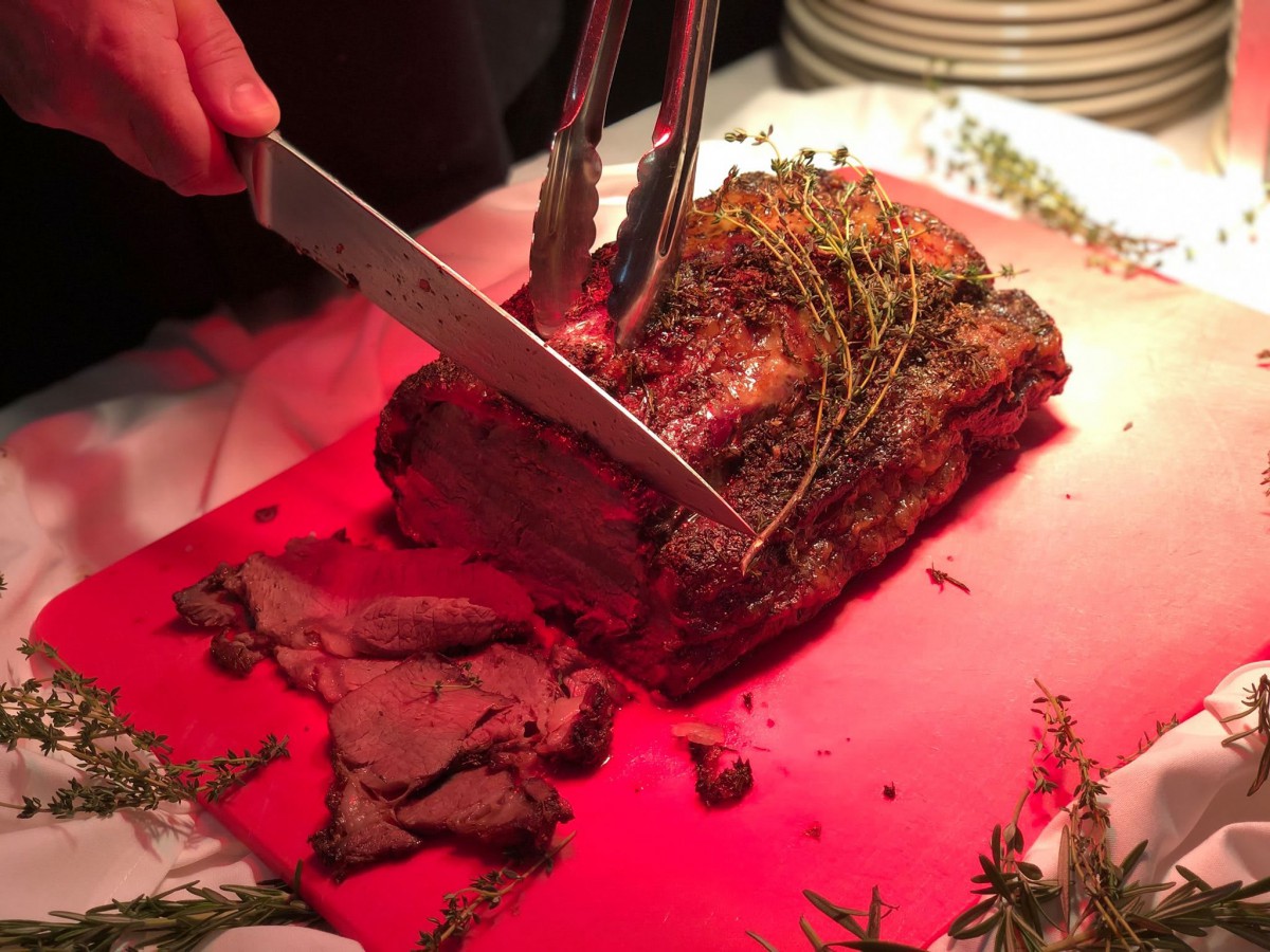A juicy roast beef being carved on a cutting board, garnished with fresh herbs.