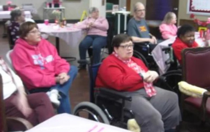 A group of people seated indoors, some in wheelchairs, engaged in a casual setting.