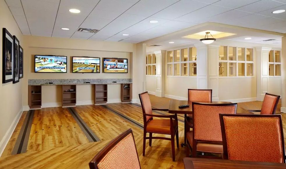A recreational indoor space featuring mini bowling alleys with seating areas and a polished wooden floor.